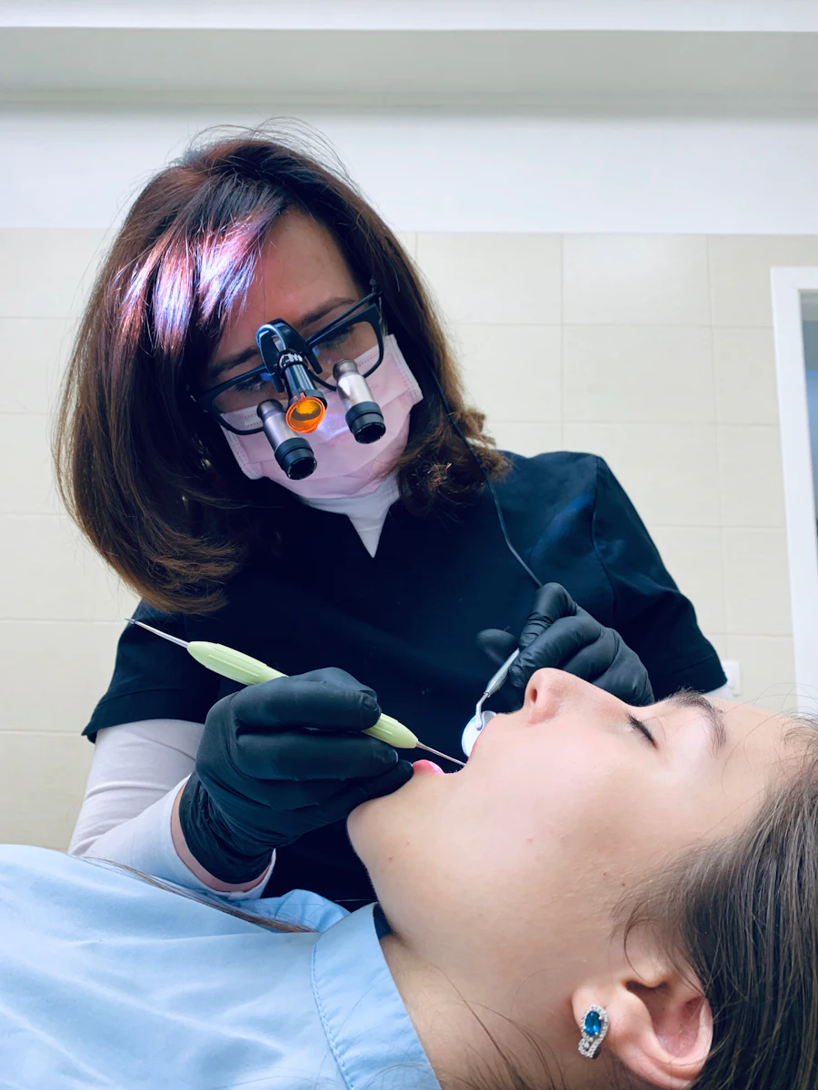 Una dentista con lupas de aumento trabaja con precisión en el diente de una paciente recostada.