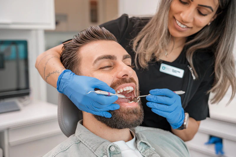 Una dentista sonriente con guantes azules revisa con un espejo los dientes de un paciente relajado.
