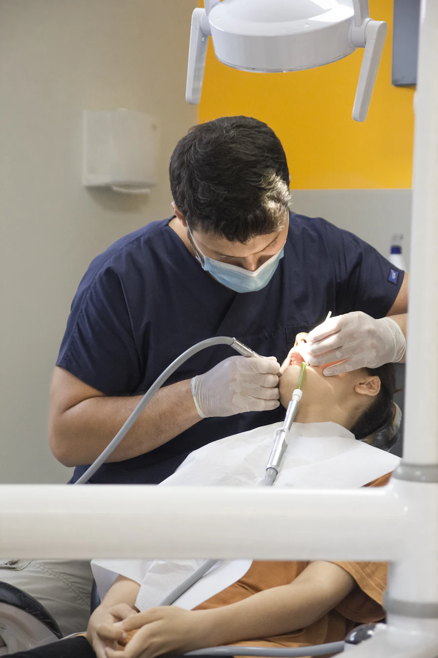 Un dentista con uniforme azul marino atiende con cuidado a un niño recostado en el sillón dental.